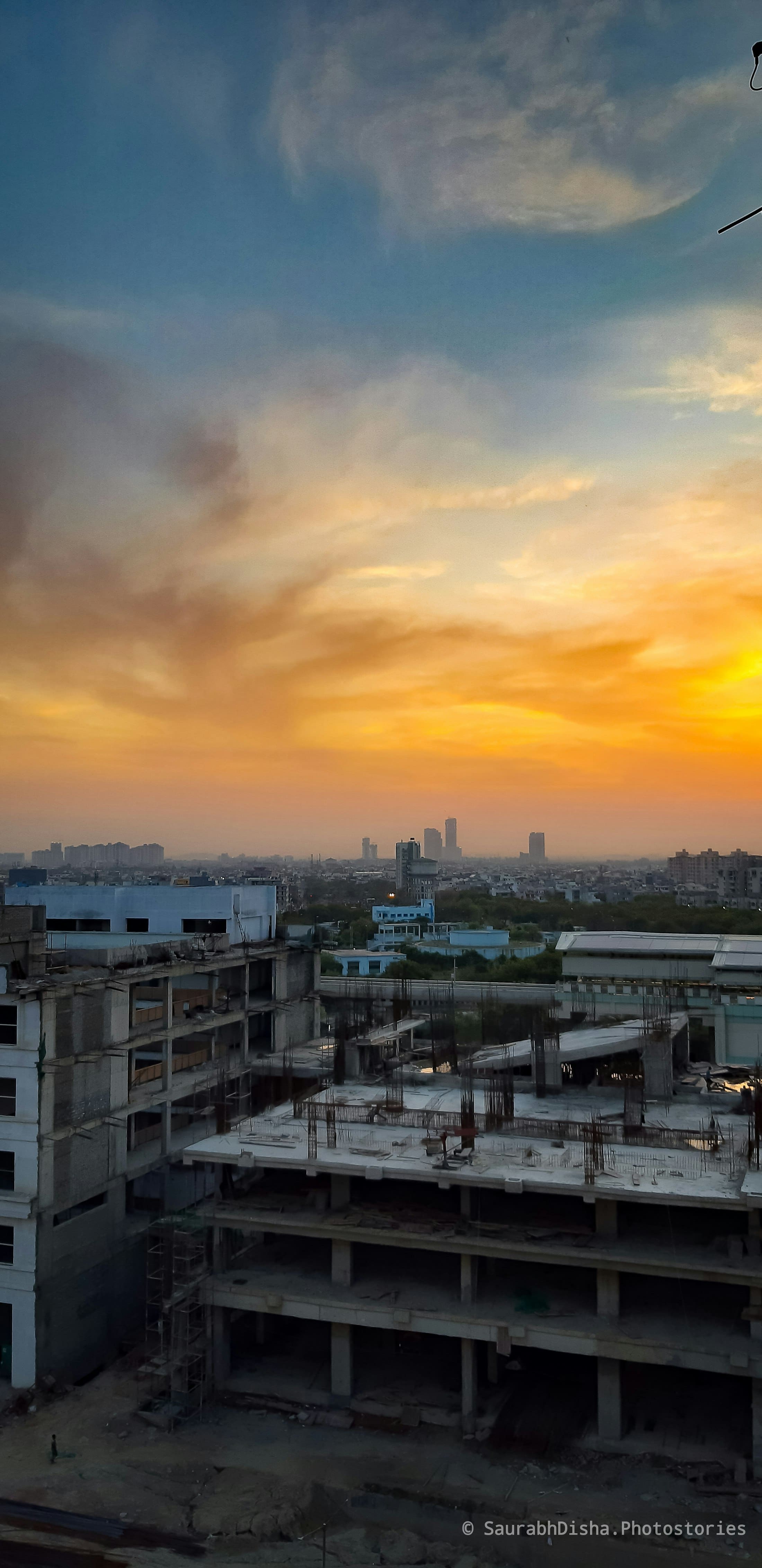 Low-rise rooftops under an orange evening sky in Noida
