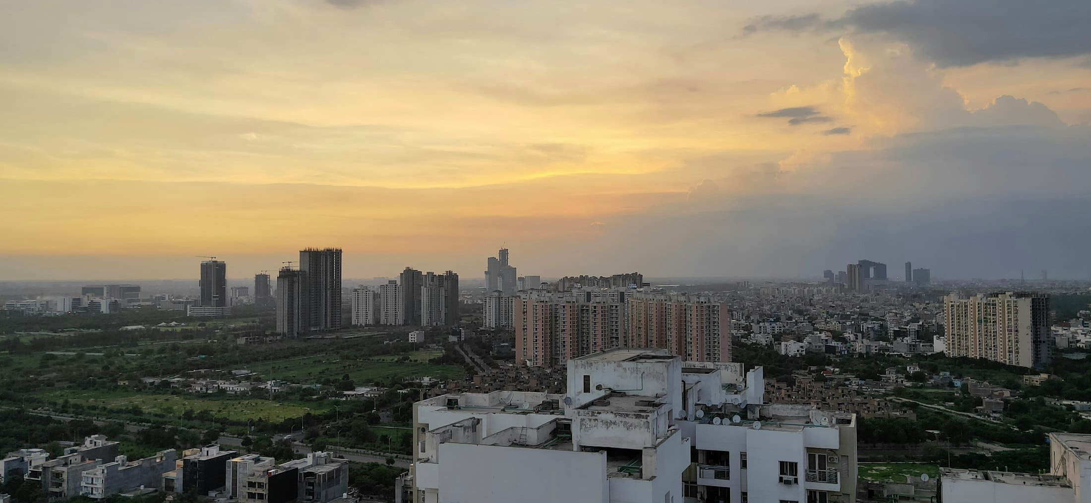 Rooftops of low-rise buildings with the Noida skyline at sunset