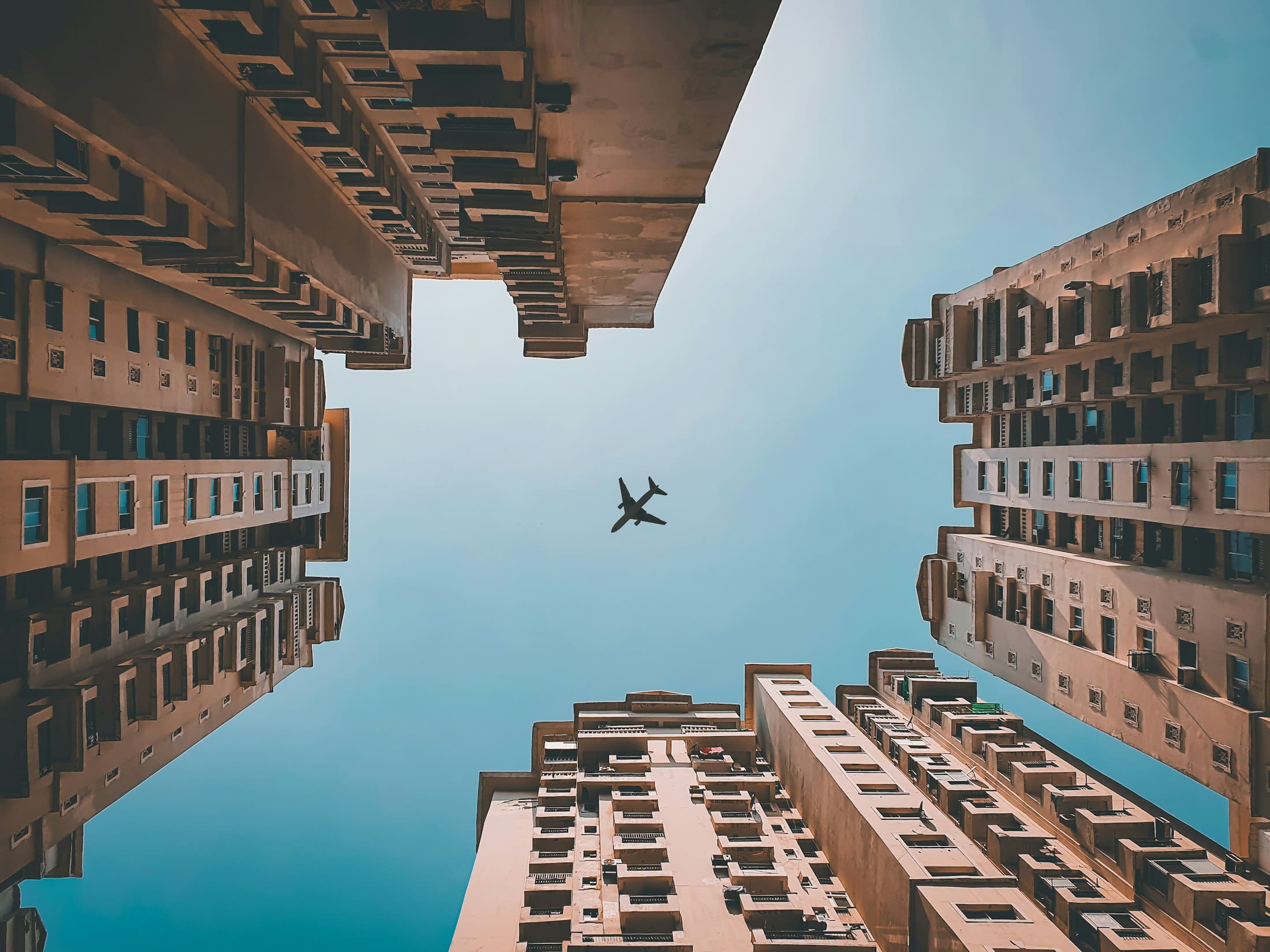 Looking up between tall buildings in Noida, with an aeroplane overhead